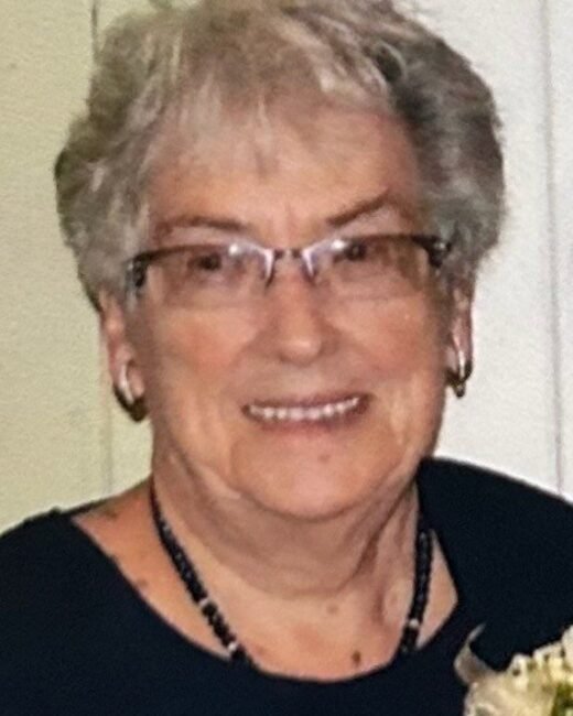 Smiling elderly person with glasses and floral boutonniere.