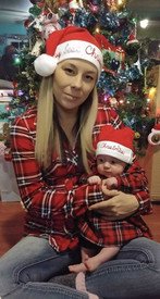 Mother and baby in Christmas hats by tree.