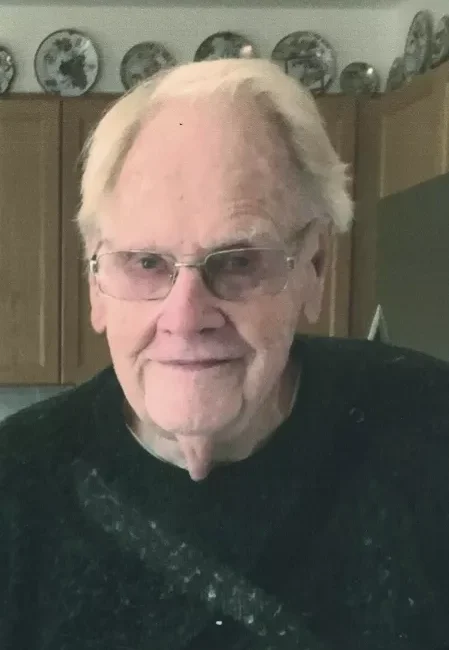 Elderly man smiling in kitchen, wearing glasses.