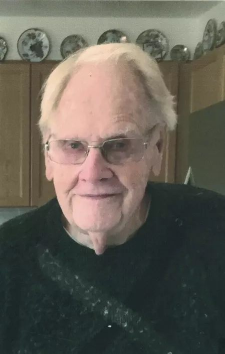 SWEEZEY Ephraim William Sweezey Elderly man smiling in kitchen, wearing glasses.