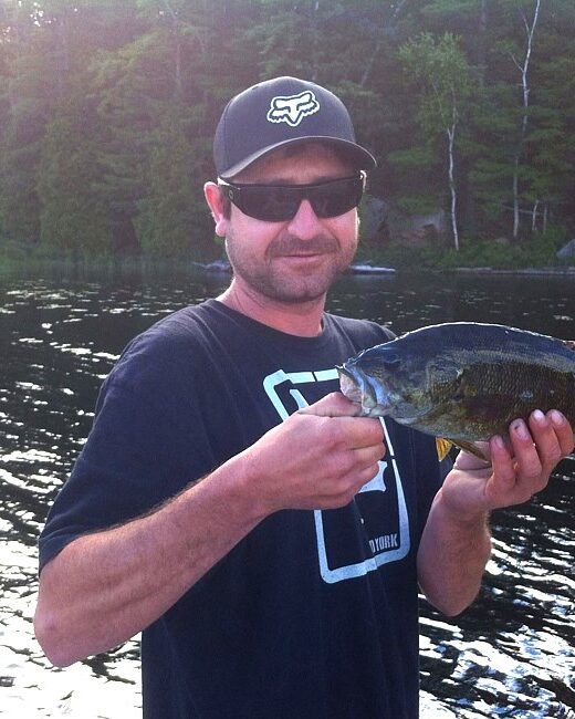 Person holding a fish by a lake.