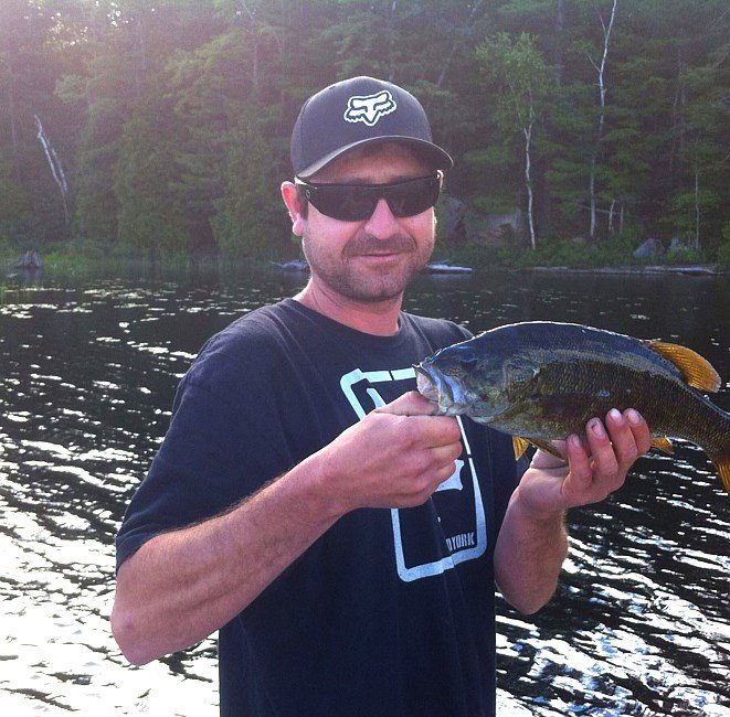 Person holding a fish by a lake.