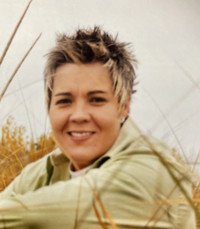 Smiling person with short hair in nature setting.