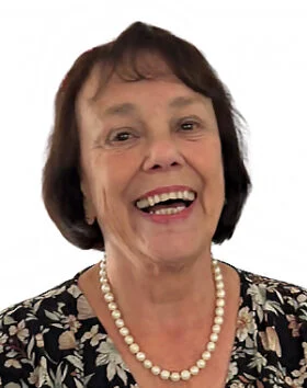 Smiling woman with floral shirt and pearl necklace.
