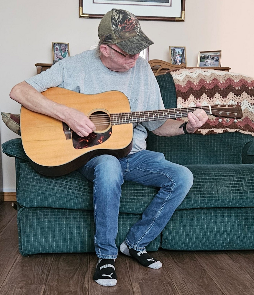 Man playing acoustic guitar on green sofa.