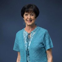 Smiling woman wearing blue cardigan on dark background.
