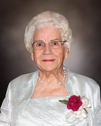 Elderly woman in formal attire with flower corsage.