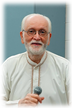 Elderly man with beard holding a microphone.