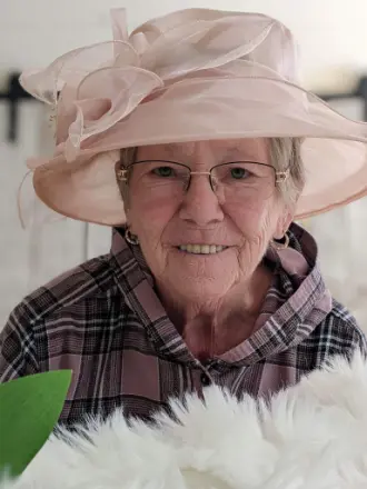 Senior woman smiling, wearing pink hat and glasses.