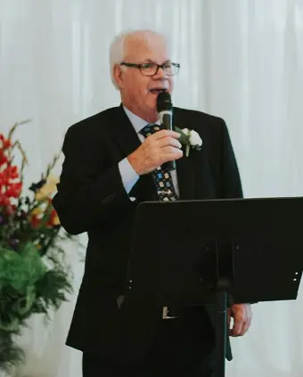 Elderly man speaking at a podium during event.