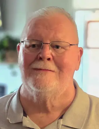 Elderly man with glasses, beard, and polo shirt.