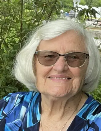 Elderly woman smiling outdoors with greenery background.