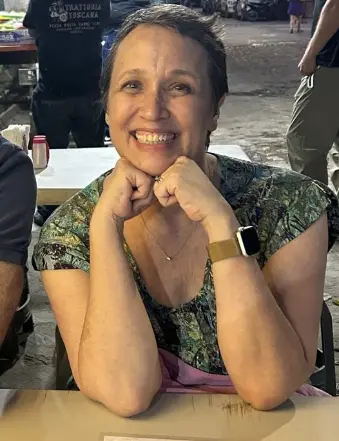 Smiling woman sitting at outdoor table in evening.