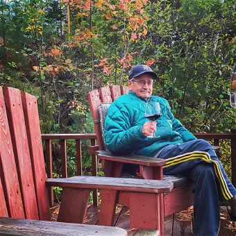 Man relaxing outdoors with wine on wooden deck.