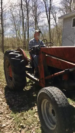 Person driving red tractor near house and trees.