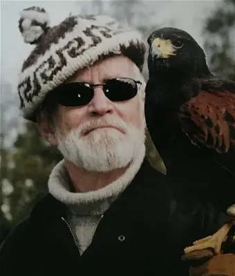 Man with a falcon on his shoulder, wearing sunglasses.