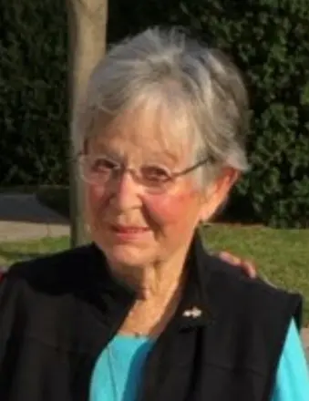 Elderly woman smiling outdoors in sunlight.