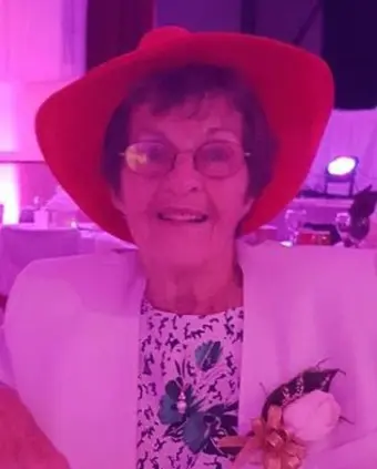 Elderly woman smiling with red hat and glasses.
