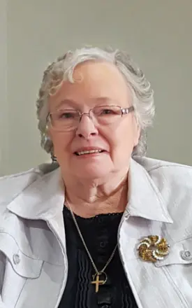 Older woman smiling, wearing glasses and white jacket.