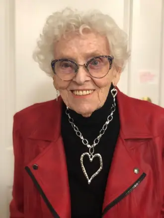 Smiling elderly woman in red jacket with heart necklace.