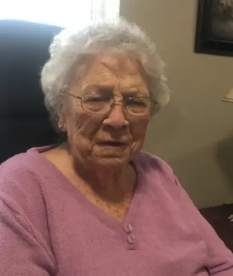 Elderly woman in purple sweater, sitting indoors.