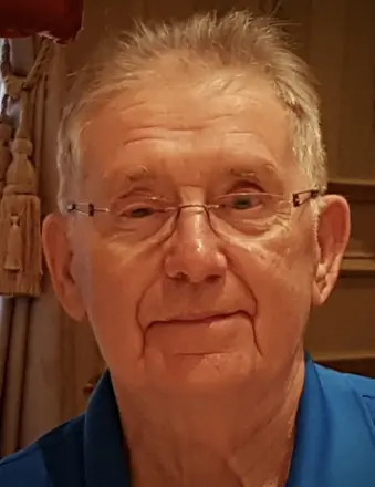 Elderly man wearing glasses and blue shirt indoors.