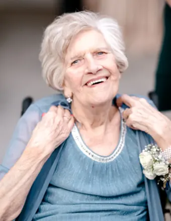Smiling elderly woman in blue dress, wearing corsage.