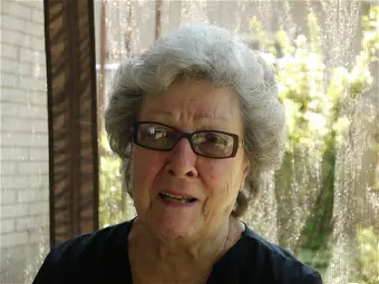 Elderly woman wearing glasses, outdoors with sunlight.