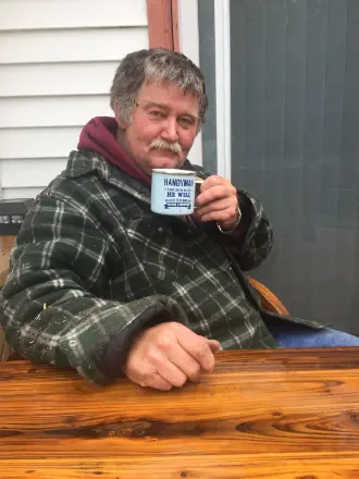 Man outdoors holding a coffee mug on wooden table