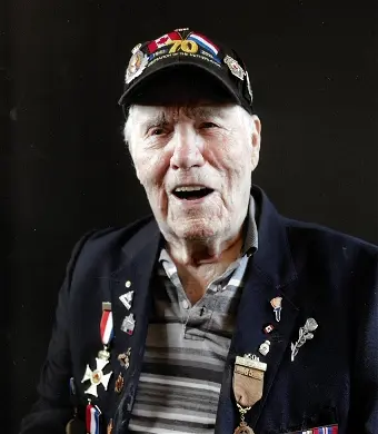 Elderly veteran wearing medal-decorated jacket and cap.