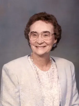 Elderly woman smiling in formal attire.
