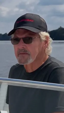 Man with sunglasses and cap on a boat.