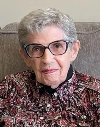 Elderly woman with glasses and patterned shirt seated