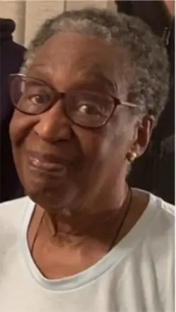 Smiling elderly woman wearing glasses and light shirt.