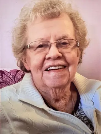 Elderly woman smiling, wearing glasses and white sweater.
