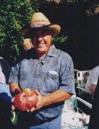 Man holding large tomato, smiling outdoors.