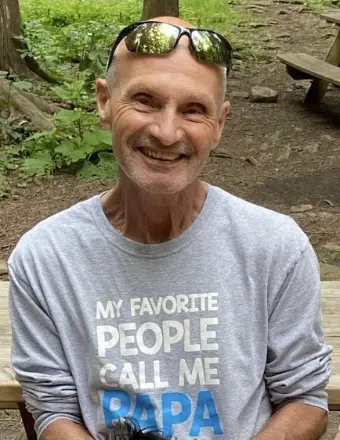 Smiling man outdoors wearing 'Papa' shirt.