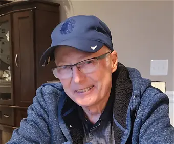 Smiling man wearing glasses and baseball cap indoors.