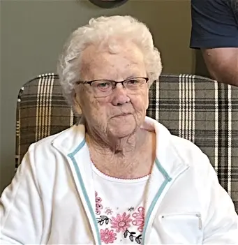 Elderly woman sitting on a plaid chair indoors.