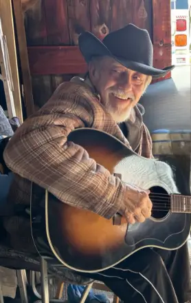 Smiling man in hat plays acoustic guitar indoors.