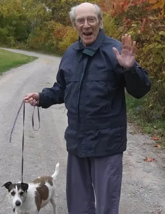 Elderly man walking dog on a tree-lined path.