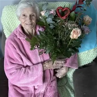 Elderly woman smiling with a bouquet of flowers.