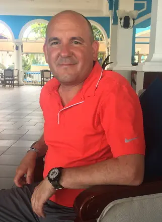 Man sitting in resort lounge with palm trees outside.
