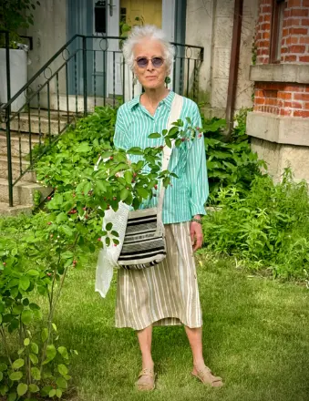 Elderly woman standing beside garden bush.