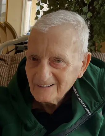 Older man smiling indoors in a green jacket.