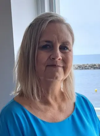 Woman in blue shirt by a seaside window.