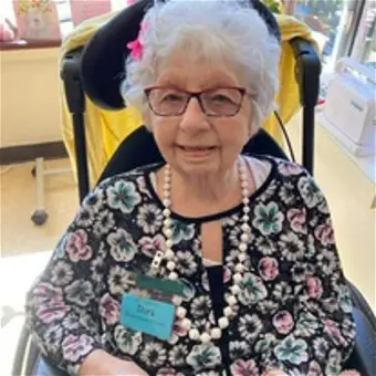 Elderly woman smiling in floral top, seated indoors.