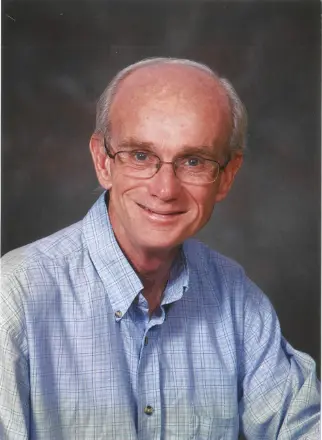 Smiling older man with glasses and blue shirt.