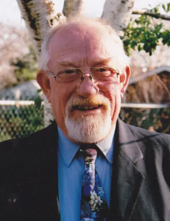 Elderly man smiling outdoors in a suit and tie.