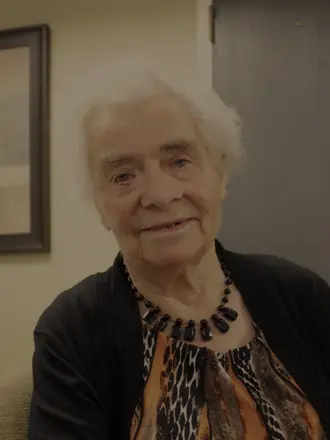 Elderly woman smiling indoors, wearing colorful blouse.
